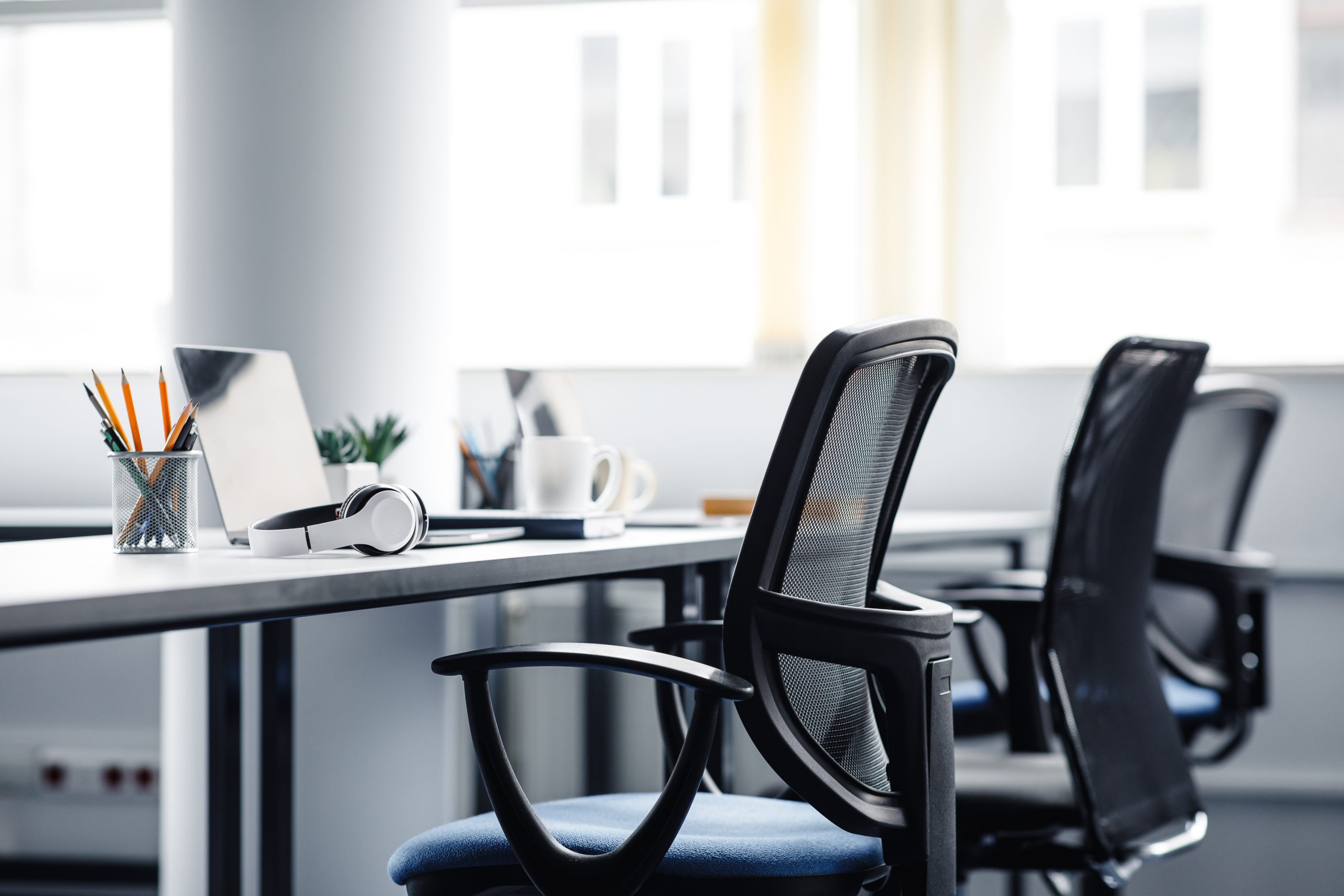 Office swivel chairs by a desk with computers, pens, and office supplies on top of it.