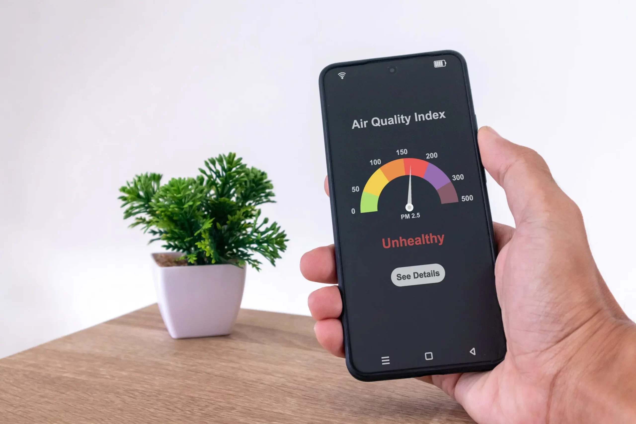 Someone holding a cell phone thats showing the air quality index of a room.